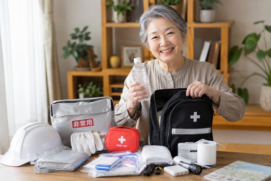 「防災の日」に非常用持ち出し袋（防災リュック）と集音器の予備バッテリー・予備パーツを点検するシニア。災害時や避難所での聞こえのトラブルを防ぐ防災ポーチの準備と、Mimitakara集音器の活用法を解説するイメージ。
