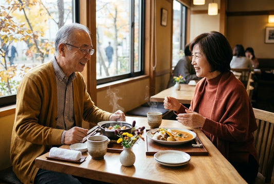 10月下旬のカフェやレストランで、温かいお茶とお料理を前に、笑顔で楽しく会話をしながら過ごしているシニアご夫婦の写真